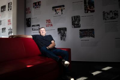 Bohuslav Štastný sedí na červeném gauči, za sebou má na zdi hostrorii pardubického hokeje