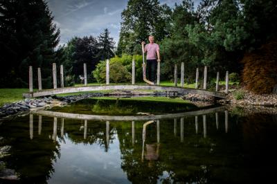 Dominik Hašek sstojí s brankářskou hokejovou hokejkou na mostku přes vodu na zahradě 