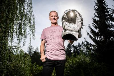 Dominik Hašek stojí s lapačkou skrz kterou prosvítají paprsky v přírodě před stromy