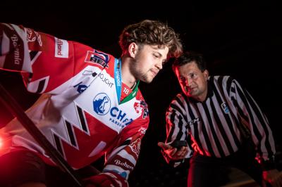 Matěj Blümel v dresu HC Dynamo Pardubce s hokejkou, vzahuje mu puk jheo otec rozhodčí