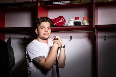 Matěj Blümel stojí před svojí skříňkou v šatně HC Dynamo Pardubice, drží hokejku, ve skříňce má pásky a hokejové rukavice 